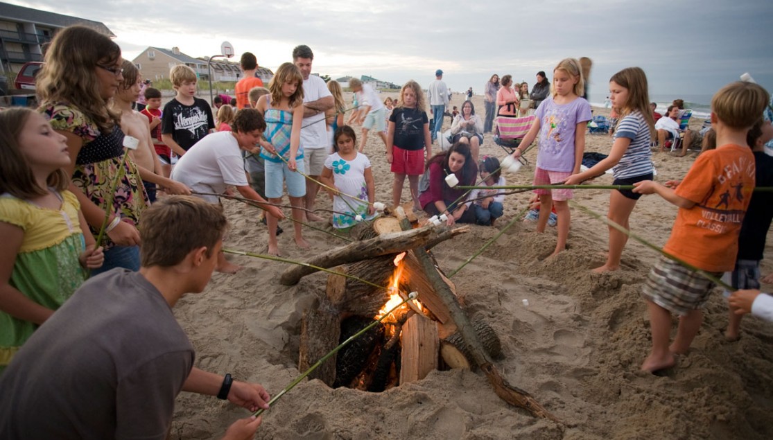 group of kids around bonfire with sticks roasting marshmallows